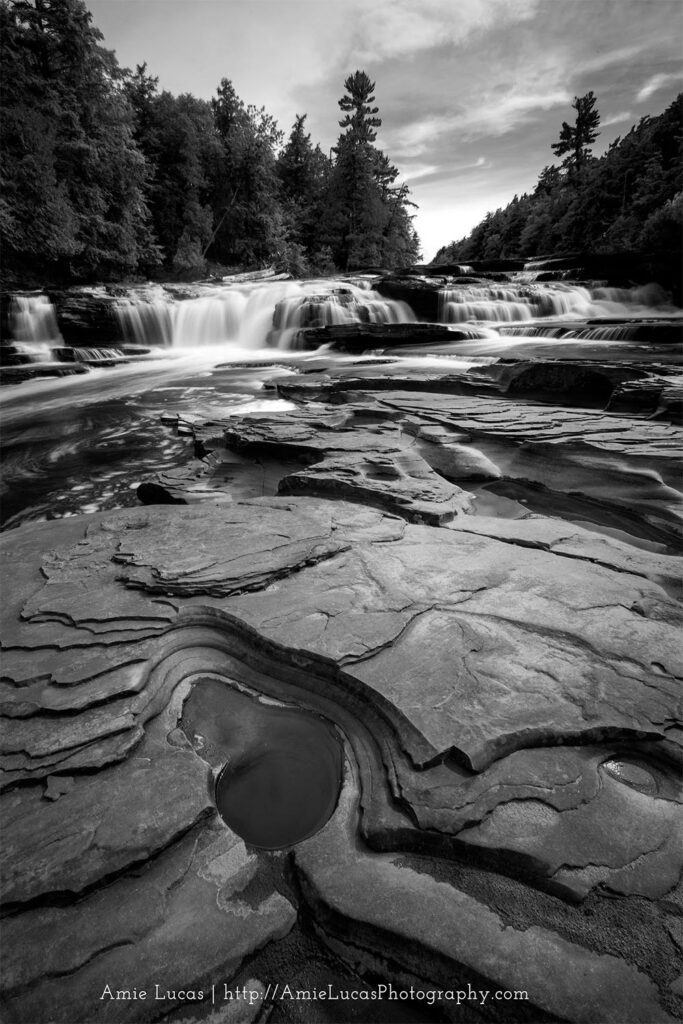 Black and white photo of a waterfall with  multiple pot holes in front of it